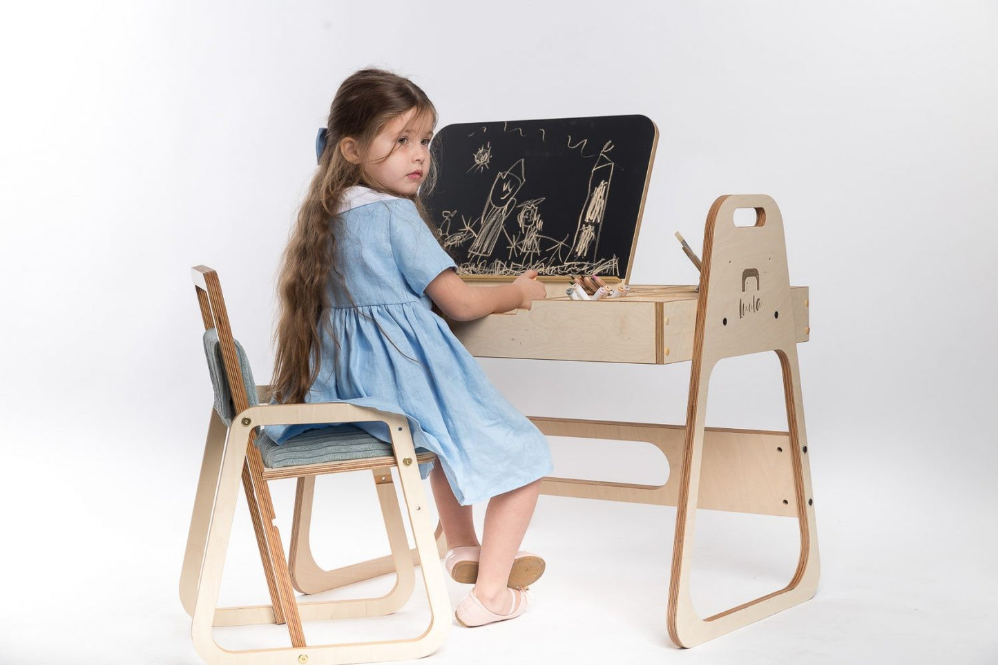 Girl in blue dress drawing on chalkboard panel at Luula Julle table