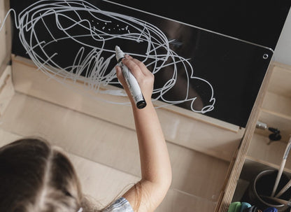 Child drawing on chalkboard surface attached to Montessori table during creative play activity
