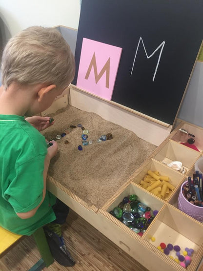 Young boy doing sensory play with small objects in table compartments