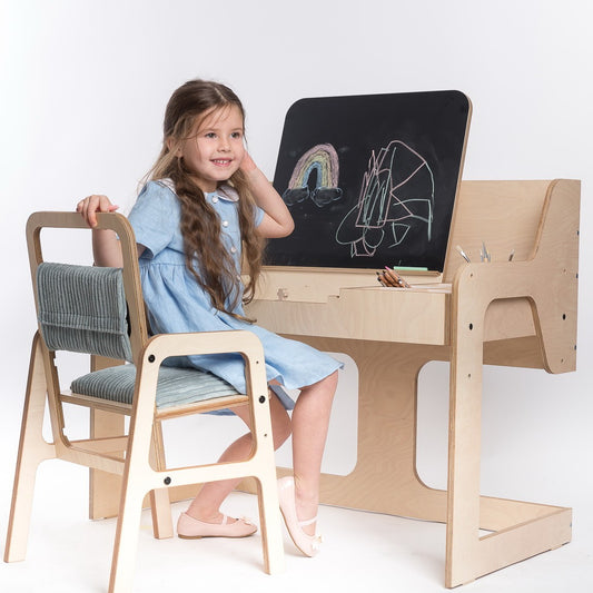 Child sitting at mint green Montessori table and chair set, drawing on blackboard