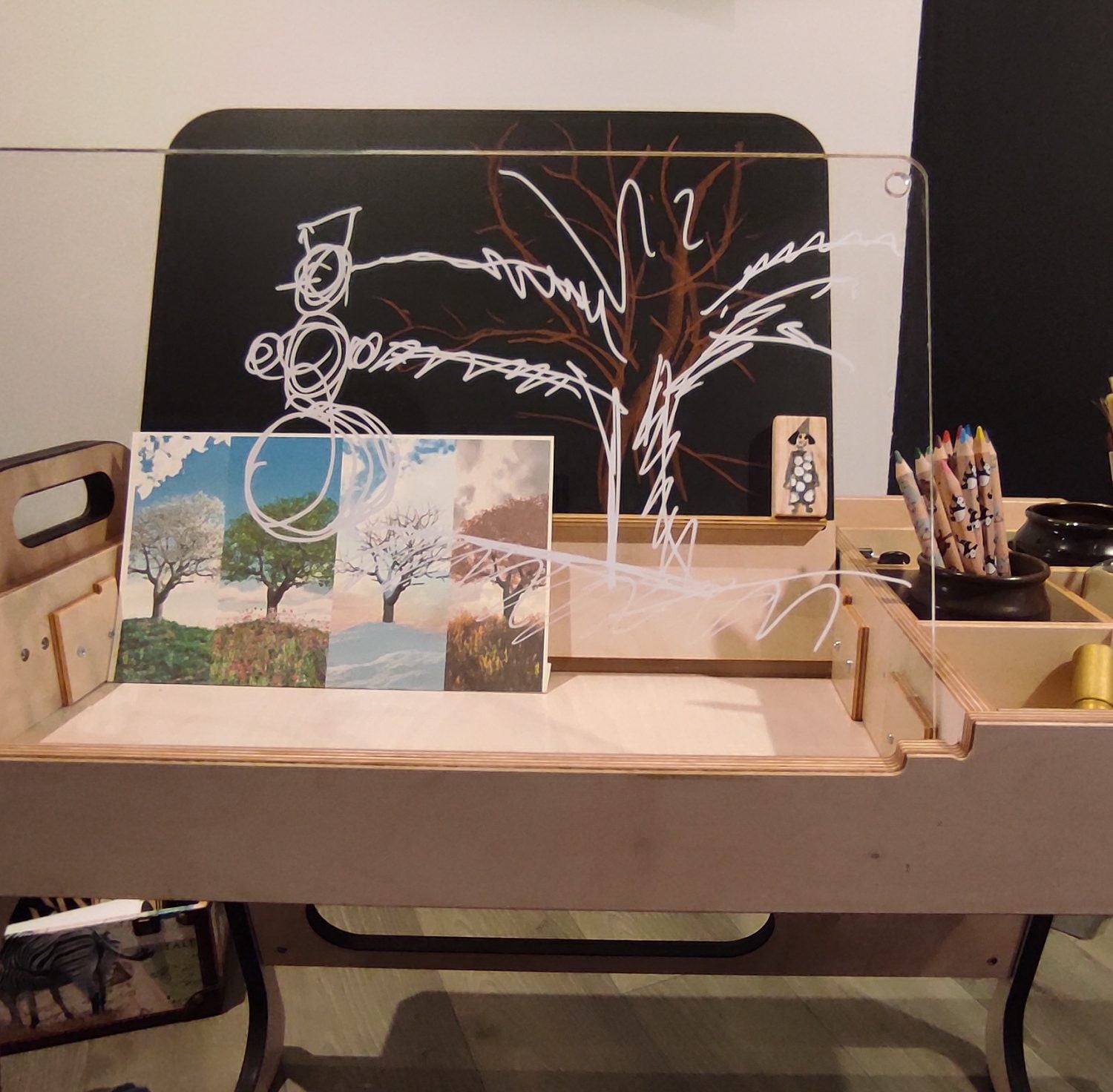 Montessori table workspace displaying artwork, chalkboard, and organized activity materials for children