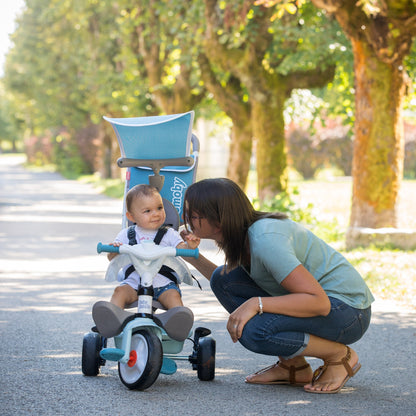 Toddler riding blue Baby Balade tricycle outdoors while parent supervises on tree-lined path