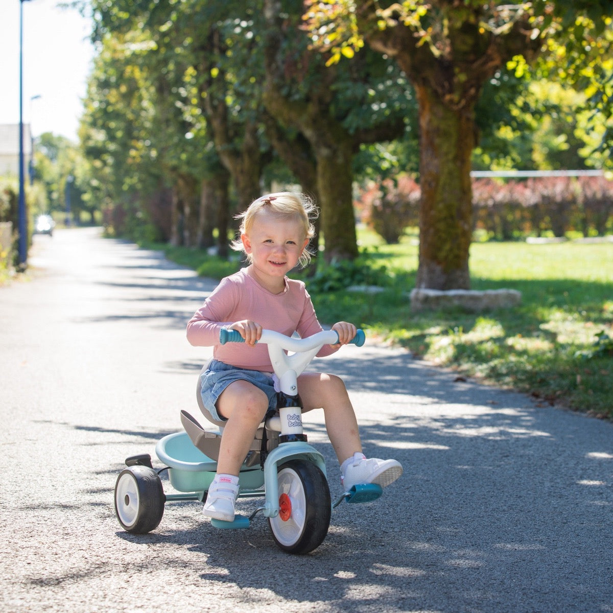 Young toddler riding blue Baby Balade tricycle independently on outdoor driveway