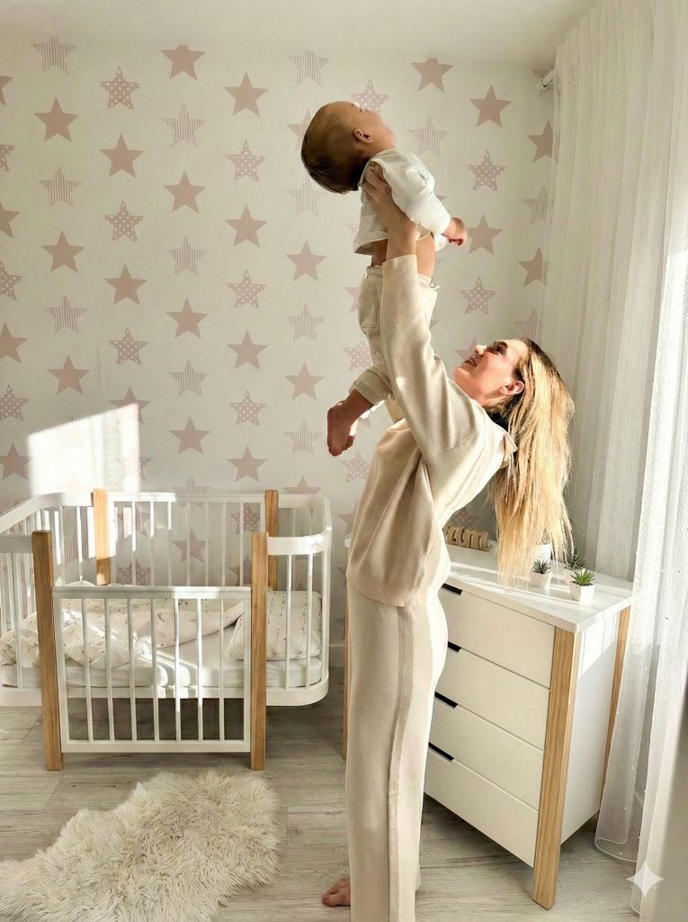 Adult lifting baby from ELIN crib showing open side panel for bedside sleep mode
