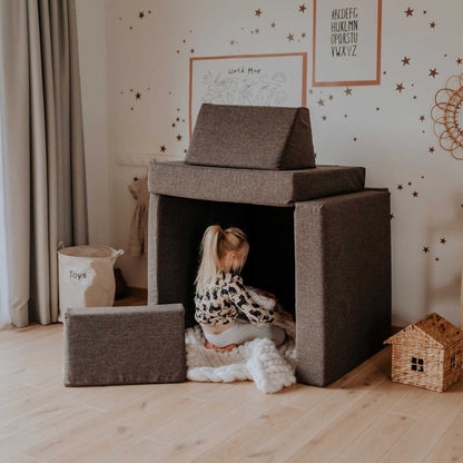 Child sitting inside dark brown foam play tent made from modular pieces in a playroom