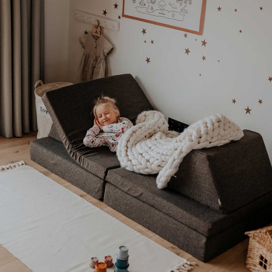 Toddler playing on dark brown foam activity mattress configured as a lounger with cushions in a playroom