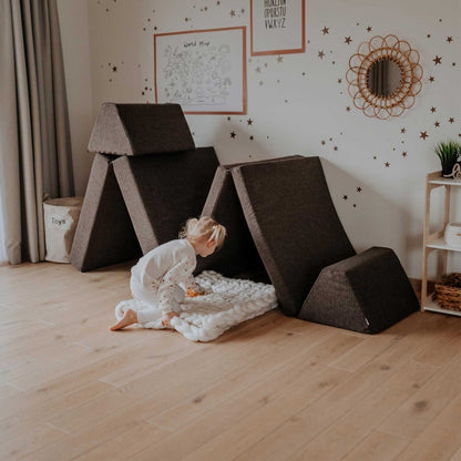 Toddler playing on dark brown modular foam furniture arranged as a play structure with multiple angles