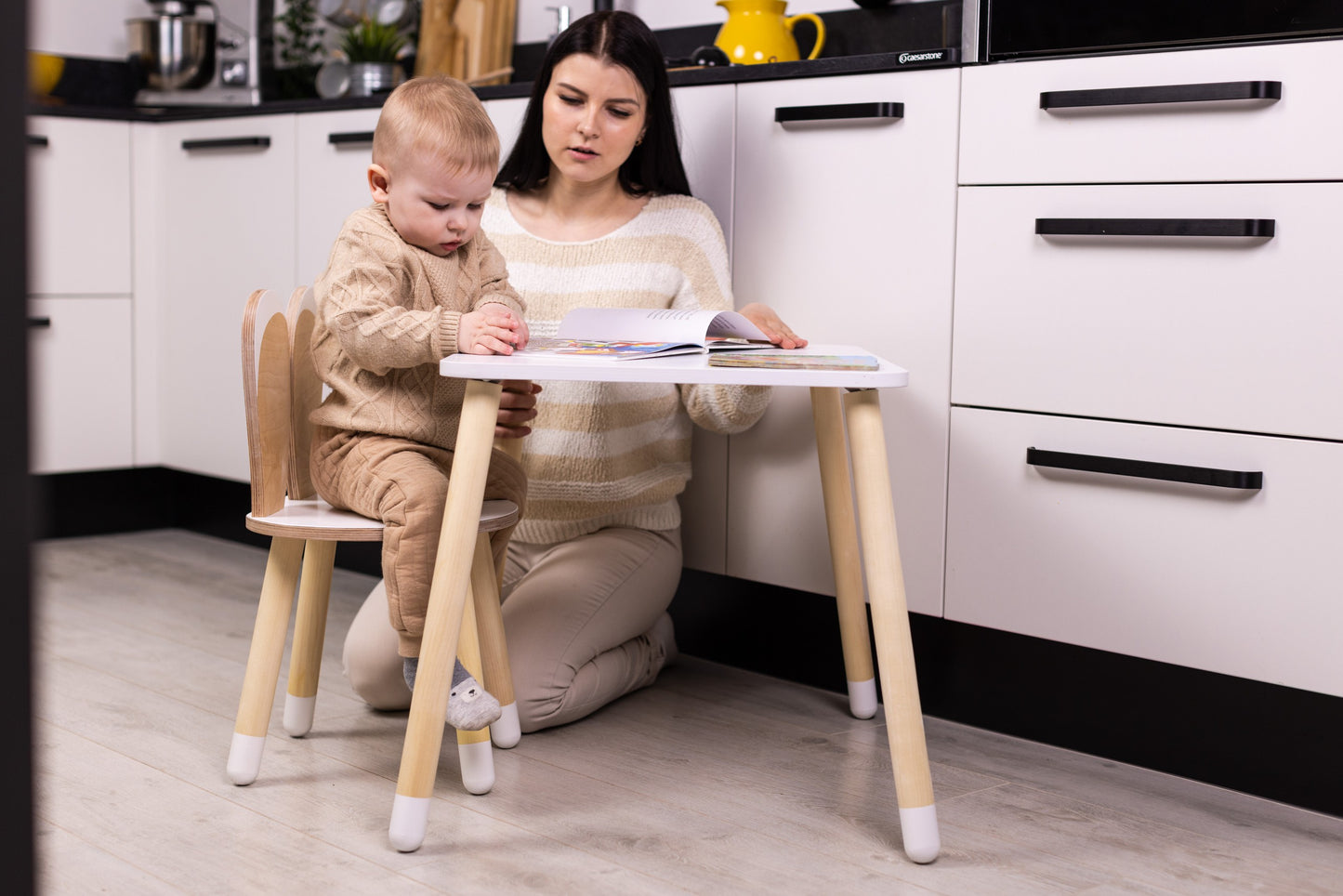 Adult kneeling beside toddler using wooden bunny table and chair set for activities