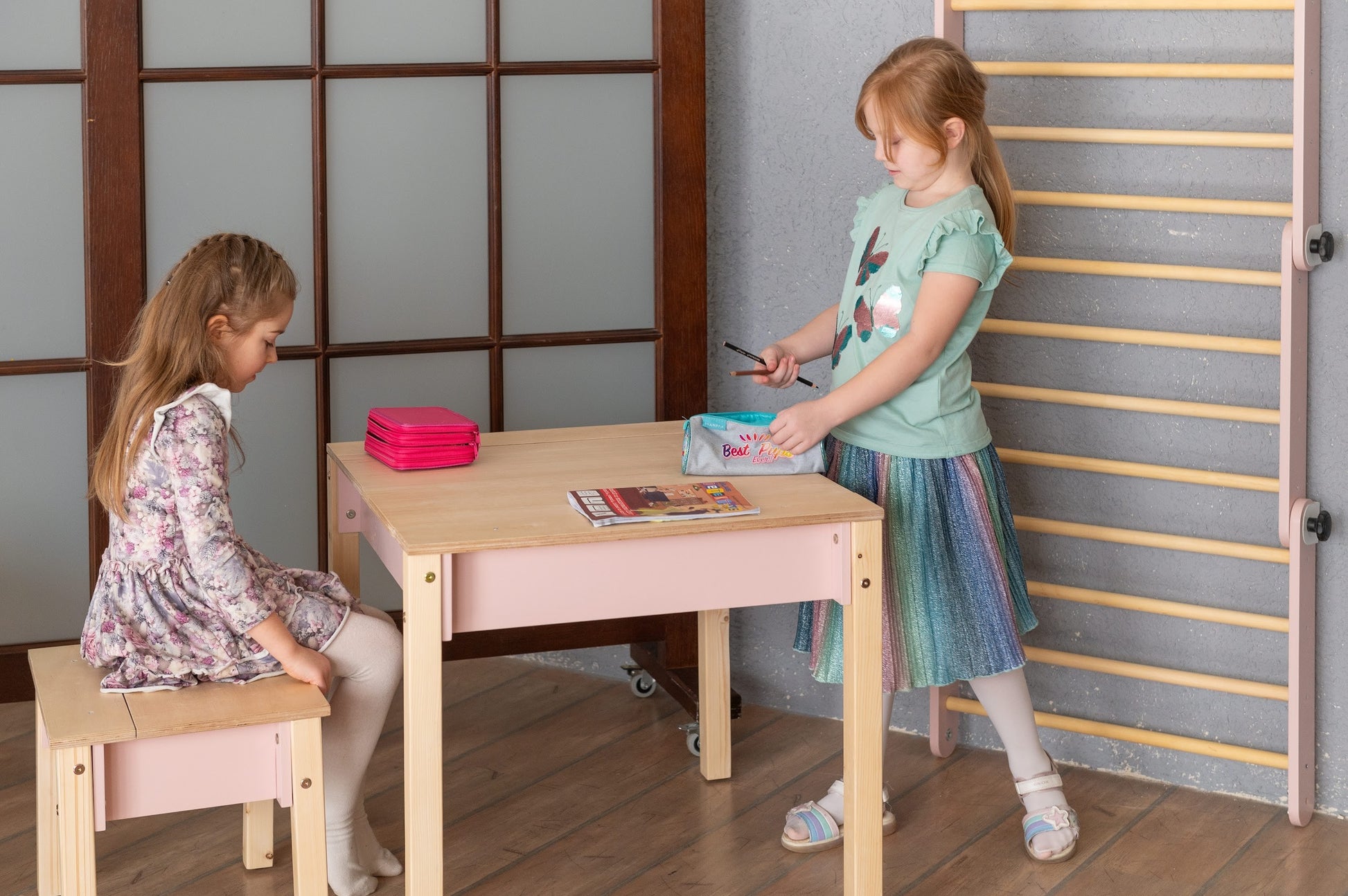 Two children at pink storage table doing crafts and activities together