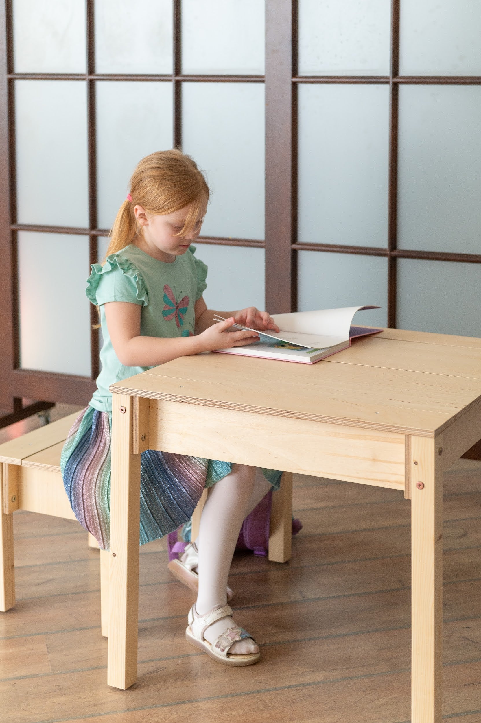 Child using natural wood table with teal storage drawer and white top