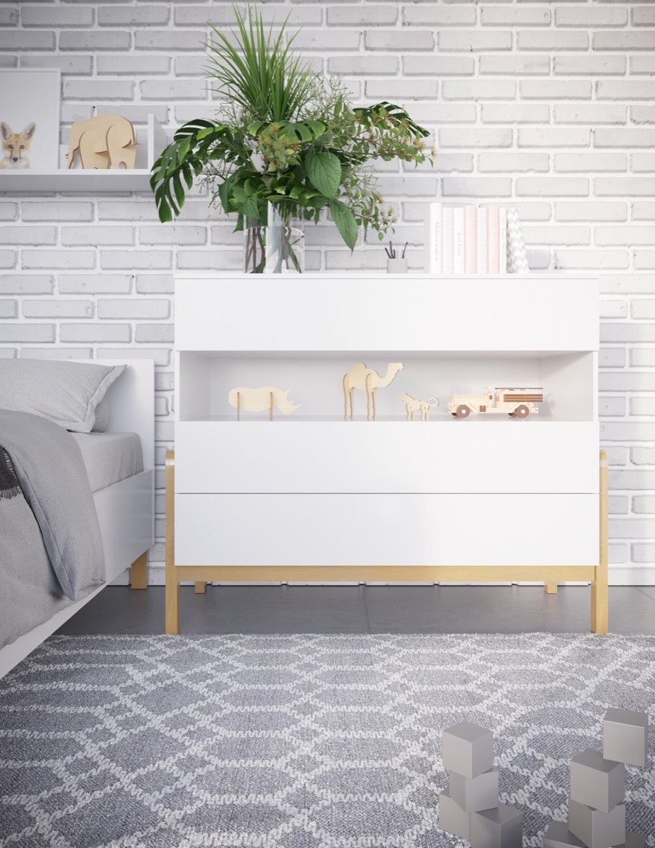White Scandinavian chest of drawers with oak legs displayed in modern nursery next to bed
