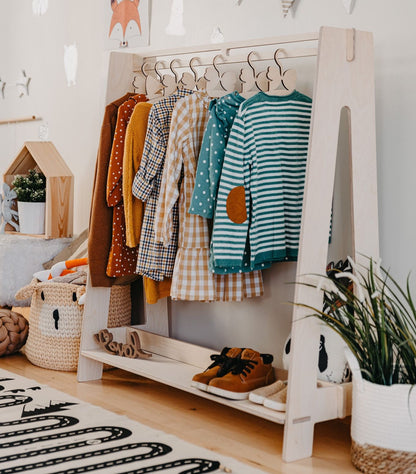 White kids dress-up rack displaying colorful clothes and shoes in a styled bedroom corner