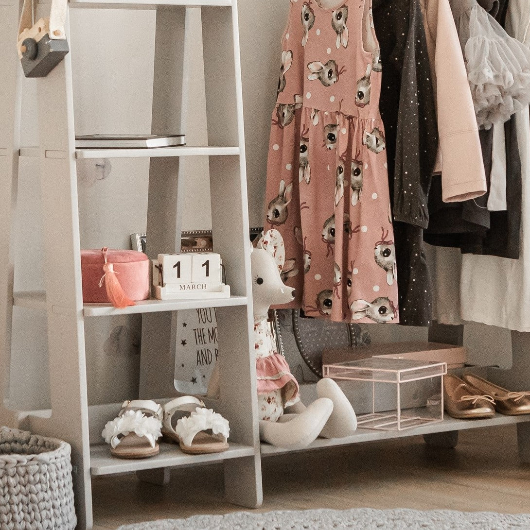 White kids clothing rack with hanging rod, multiple shelves, and shoes on base