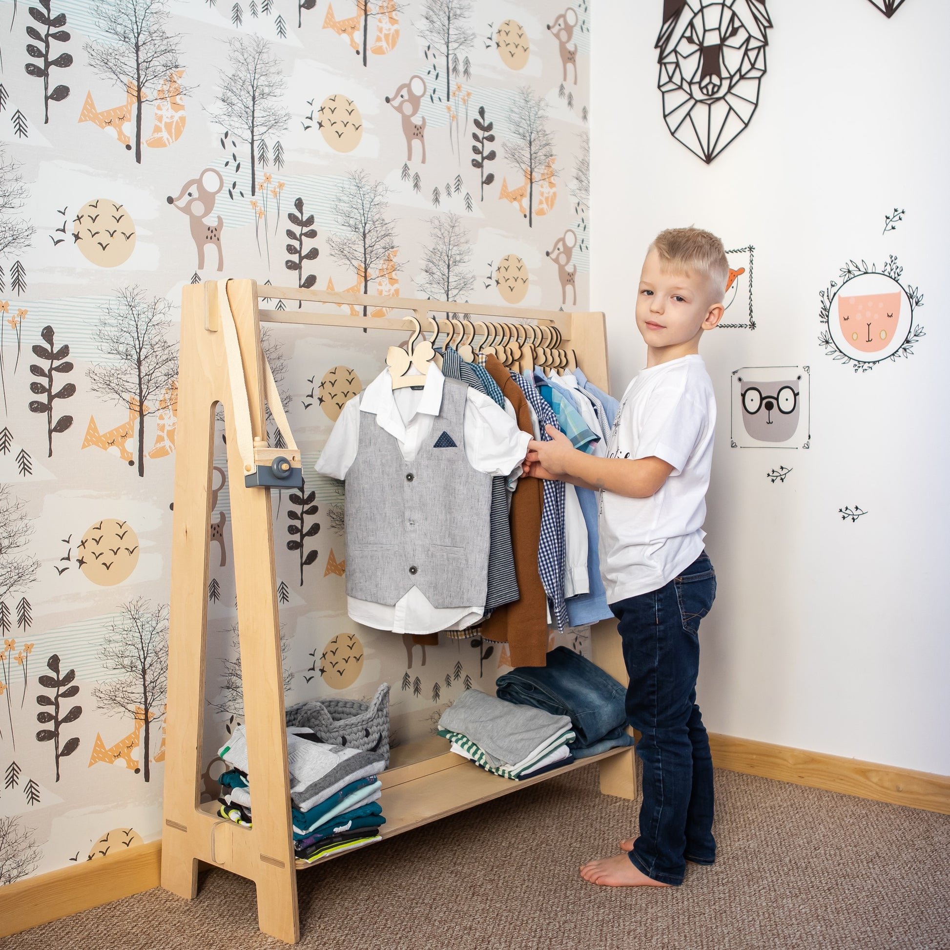 Young child selecting clothes from natural wood Montessori kids clothing rack in bedroom