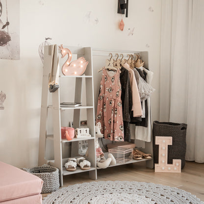 White wooden dress-up rack with shelves, clothes hangers, and storage in light nursery room