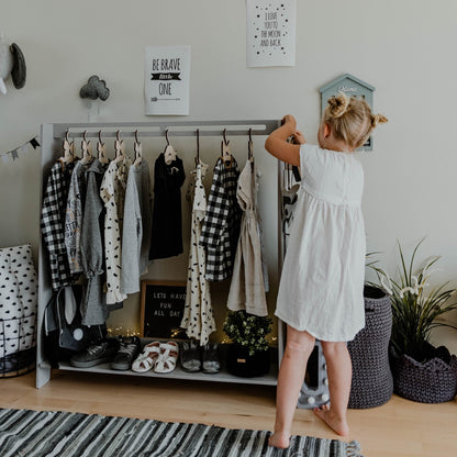 Grey kids clothing rack displaying patterned clothes and shoes, child reaching for garments