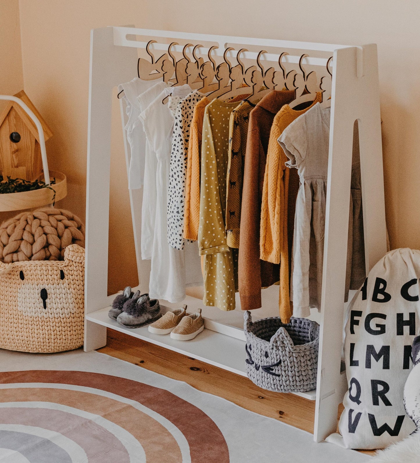 White Montessori kids clothing rack filled with colorful dresses and wooden hangers in a warm bedroom