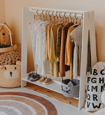 White Montessori kids clothing rack filled with colorful dresses and wooden hangers in a warm bedroom
