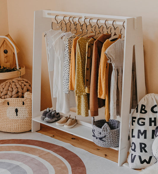 White Montessori kids clothing rack filled with colorful dresses and wooden hangers in a warm bedroom