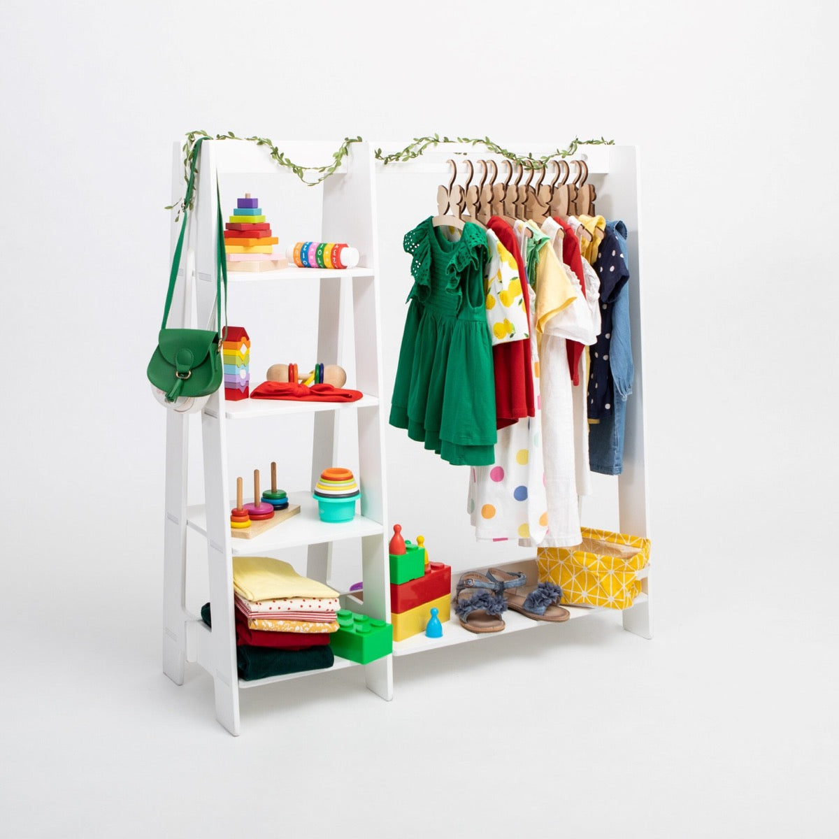 White Montessori clothing rack with shelves displaying toys, clothes, and accessories