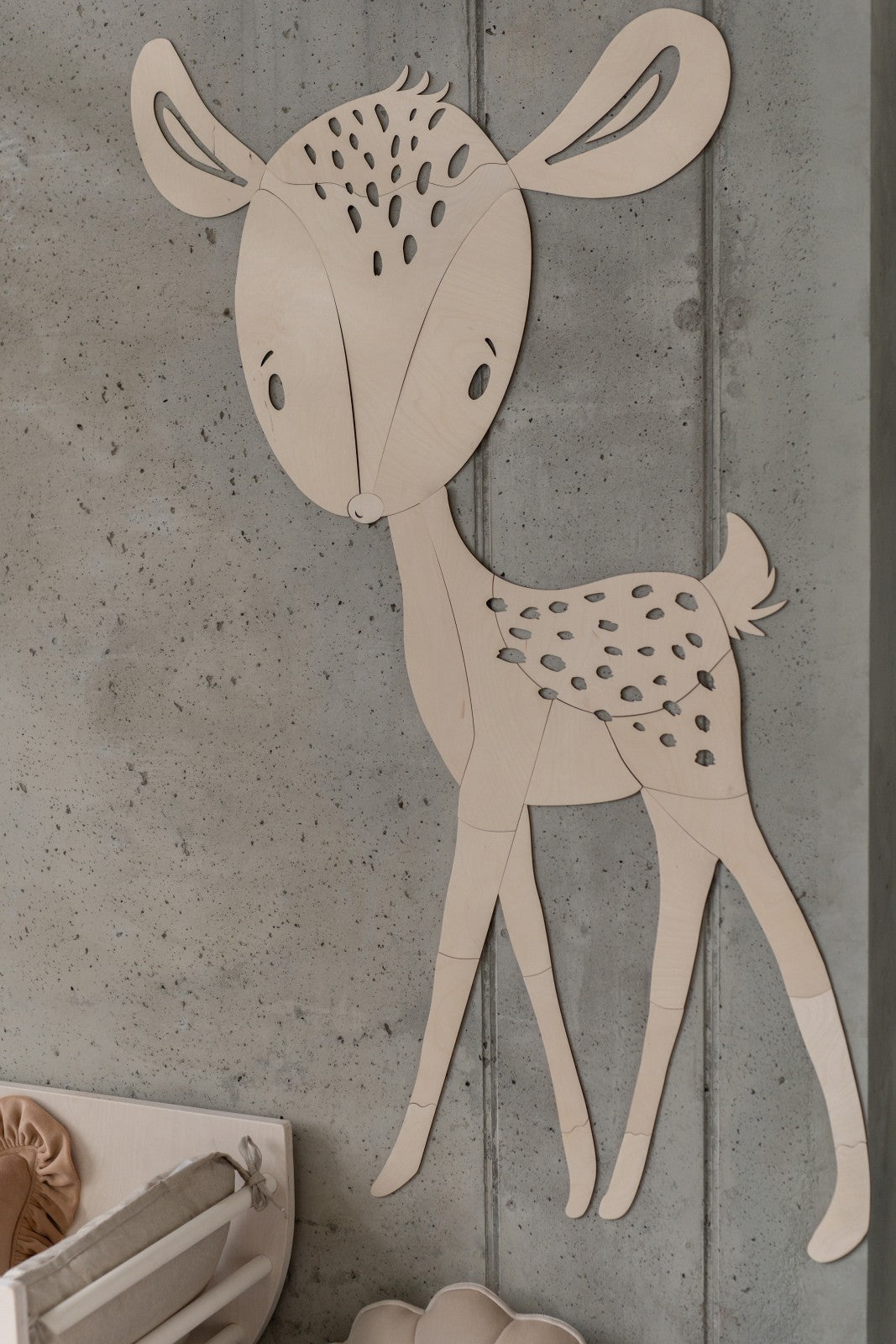 Wooden deer wall decoration with spotted coat and curved ears on concrete wall
