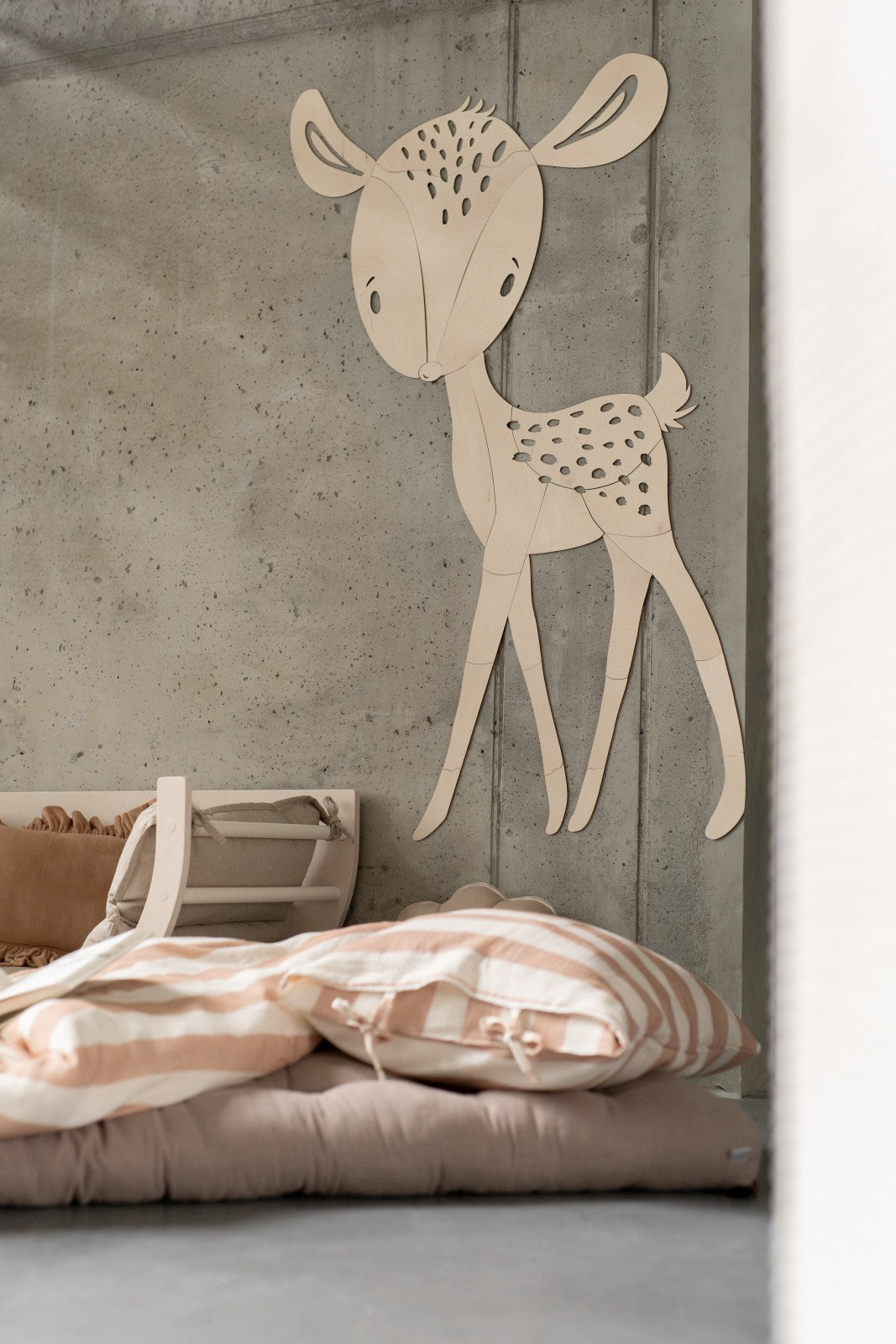 Wooden deer wall art mounted on concrete wall above pink striped bedding