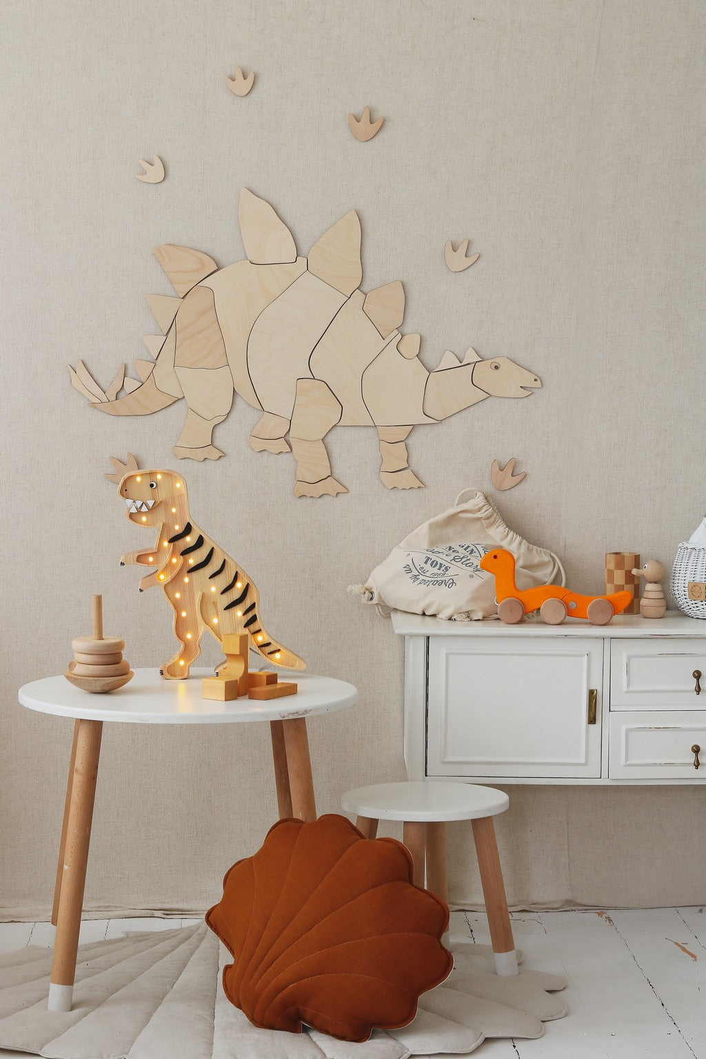 Assembled wooden stegosaurus wall art with footprint decals and wooden dinosaur toy on shelf