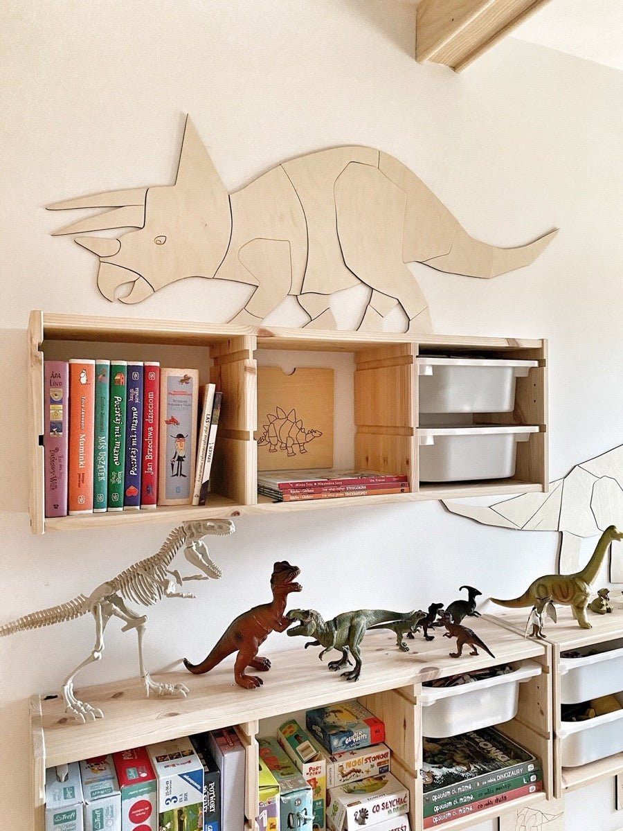 Triceratops wooden wall puzzle mounted above storage cubbies with books and dinosaur toys on shelf