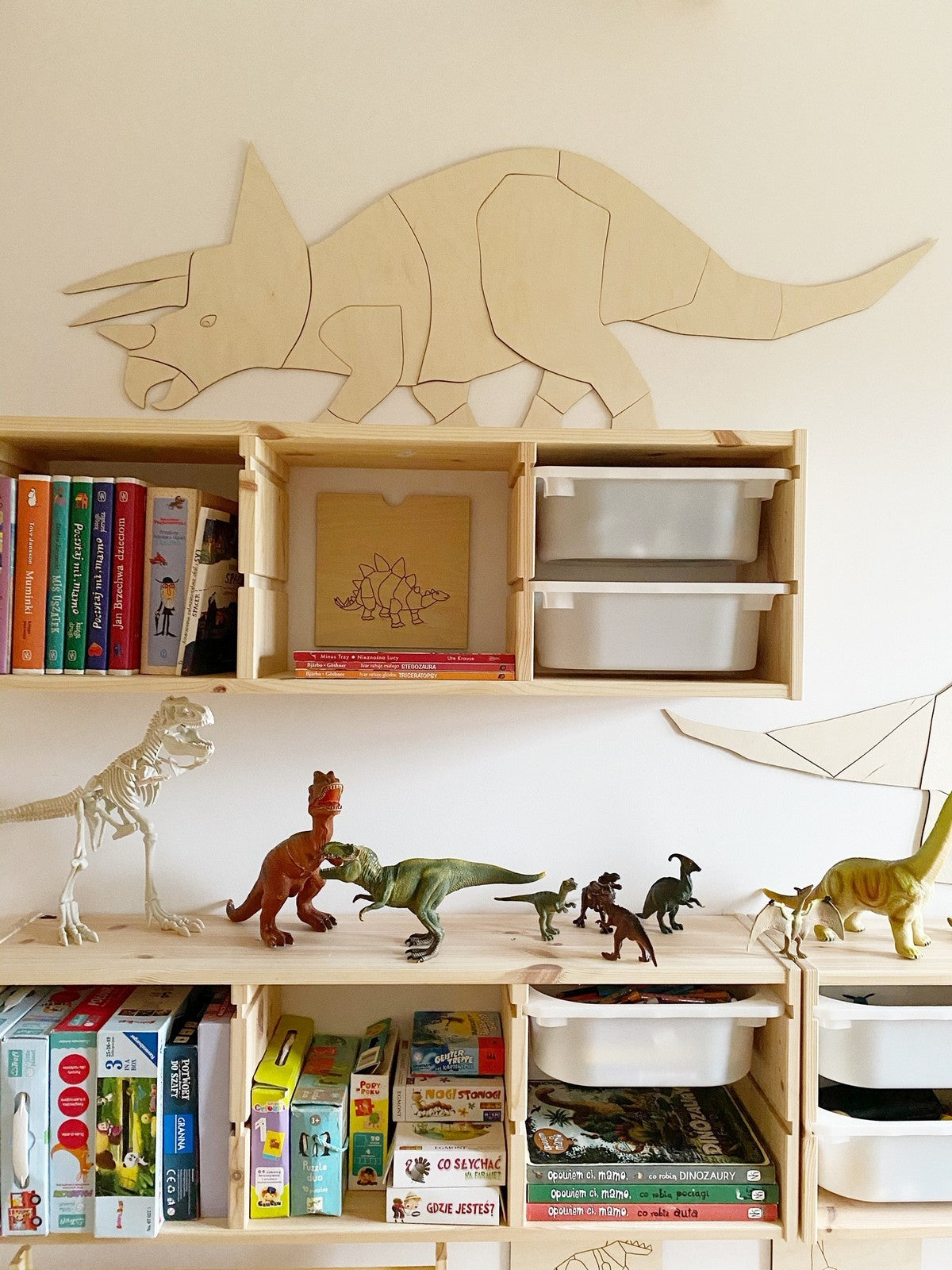 Left-facing wooden triceratops wall decoration above storage unit with children's books and toys