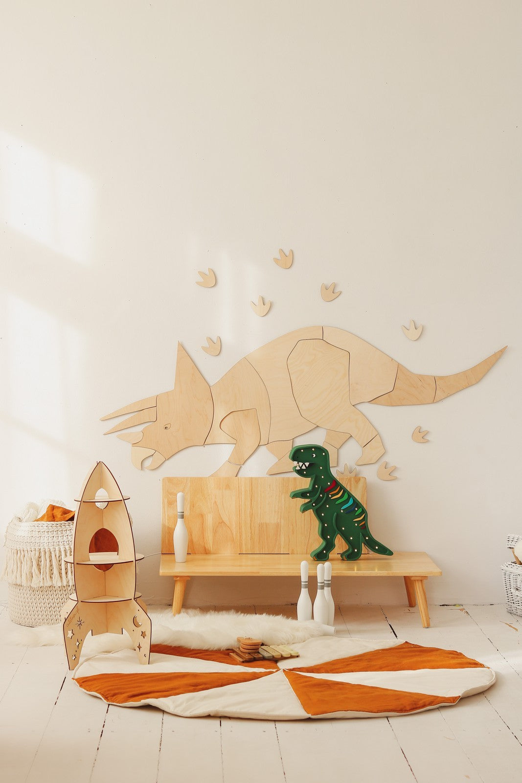Wooden triceratops wall art in playroom setting with wooden play bench, rocket toy, and dinosaur figurines
