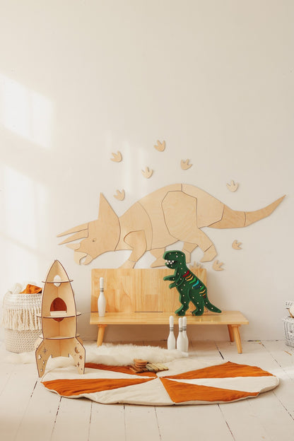 Wooden triceratops wall art in playroom setting with wooden play bench, rocket toy, and dinosaur figurines