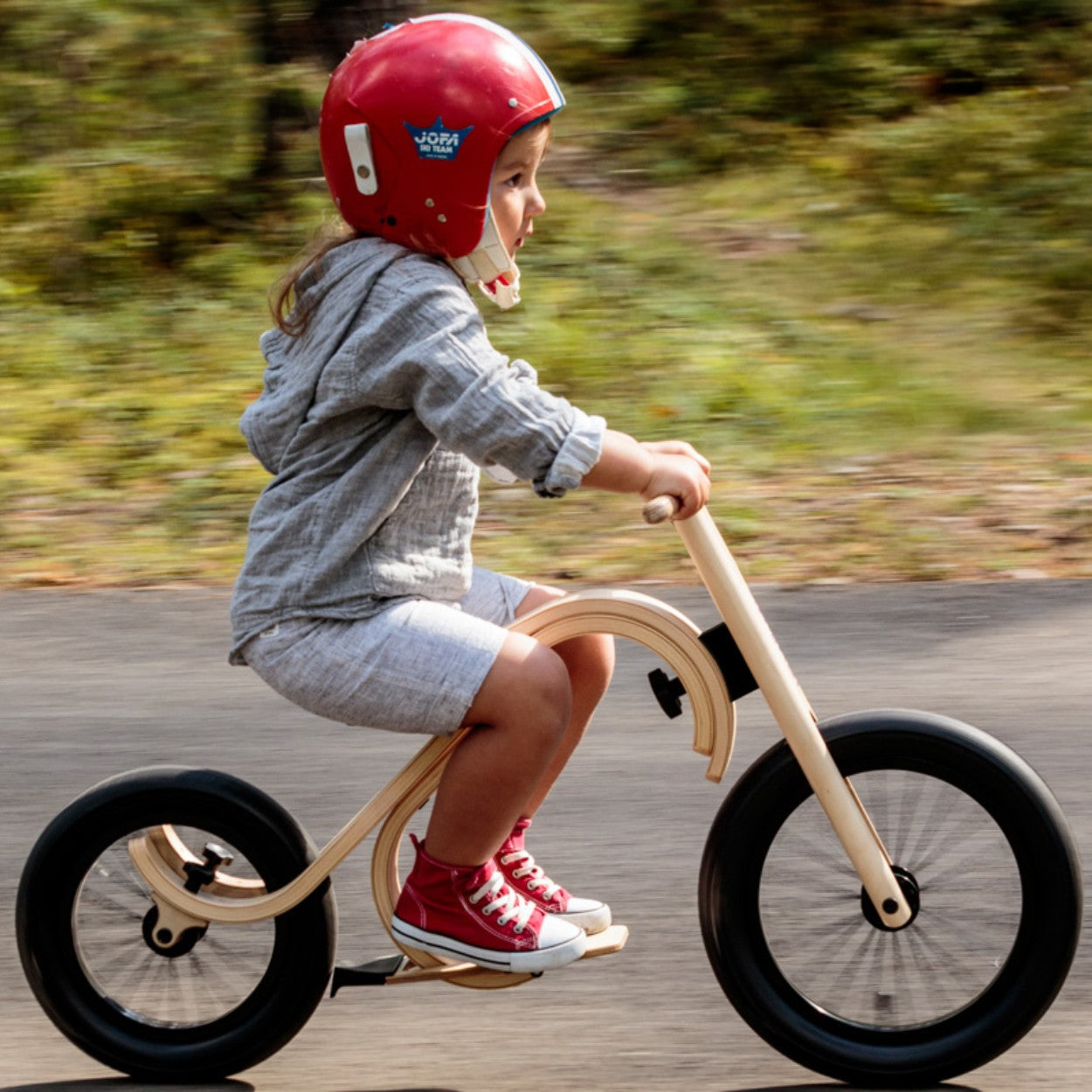 Child riding leg&go balance bike downhill wearing red helmet and using footrest add-on for stability