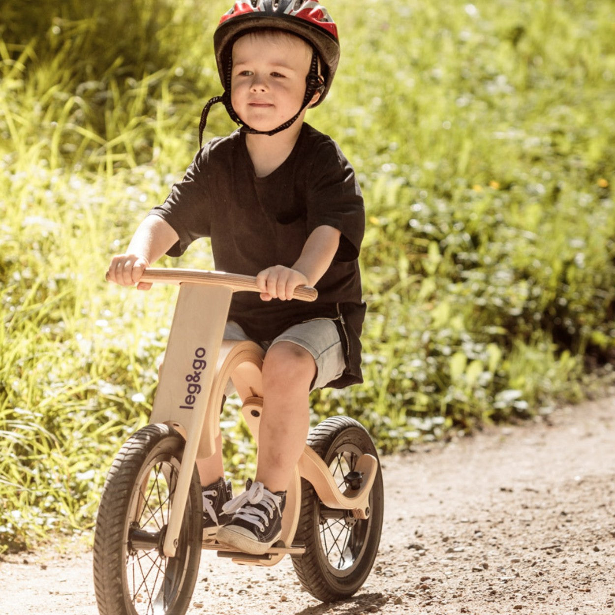 Young child on leg&go balance bike with footrest attachment in outdoor grassy setting