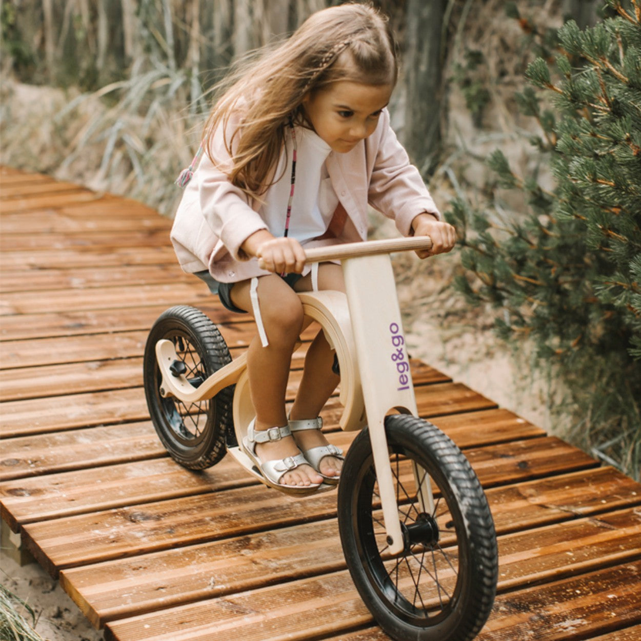Girl using leg&go balance bike with footrest brake add-on on wooden boardwalk path