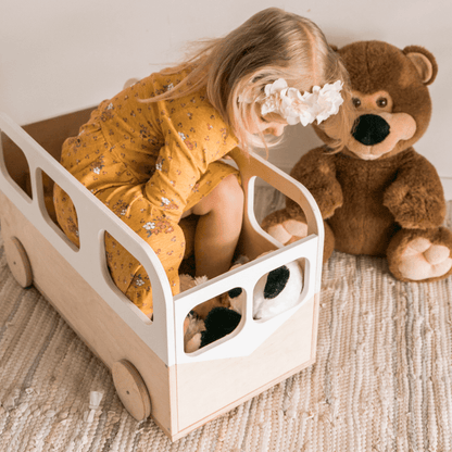 Child playing in wooden bus toy storage box with stuffed animals and toys inside