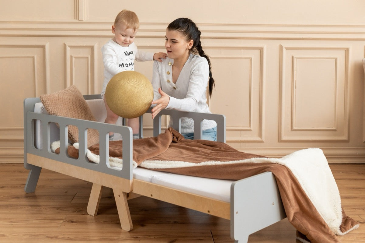 Baby standing on gray Family-scl growing bed with mother – shows child-safe design and bed height for toddlers