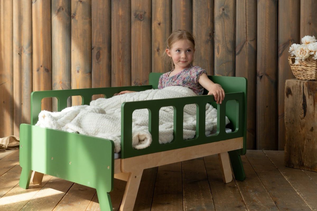Girl sitting on green Family-scl extendable growing bed – kids bed in rustic wood interior