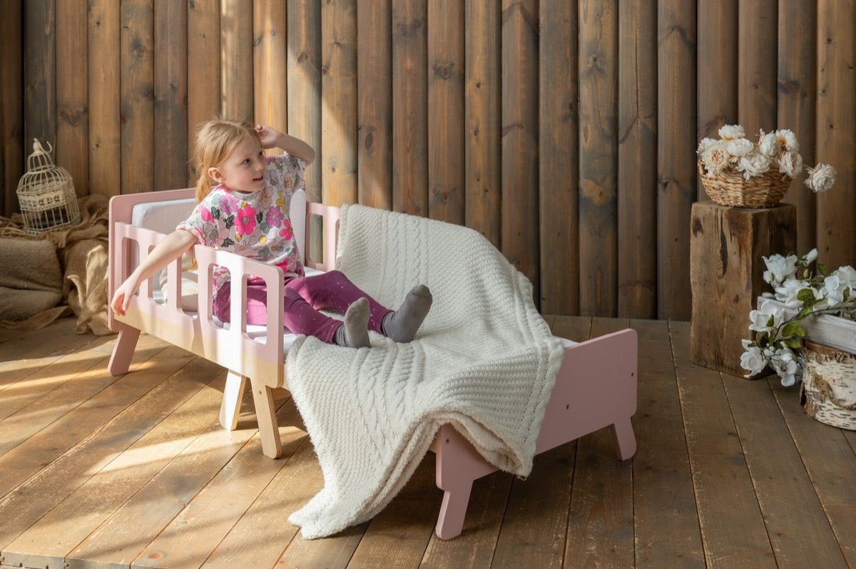 Girl sitting on pink Family-scl growing bed in sofa mode – convertible kids bed and sofa in one