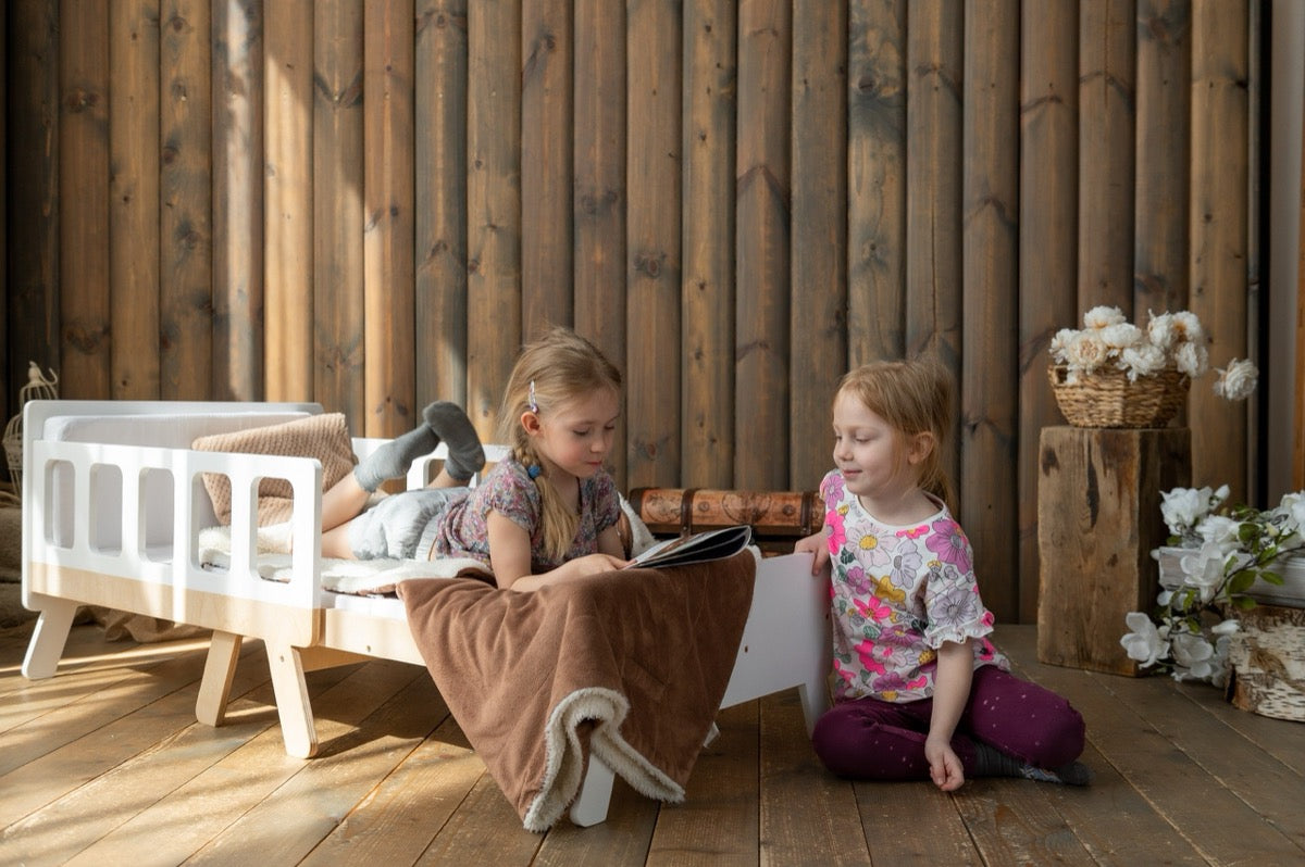 Girls reading near white Family-scl growing bed – kids extendable bed used as comfortable reading nook