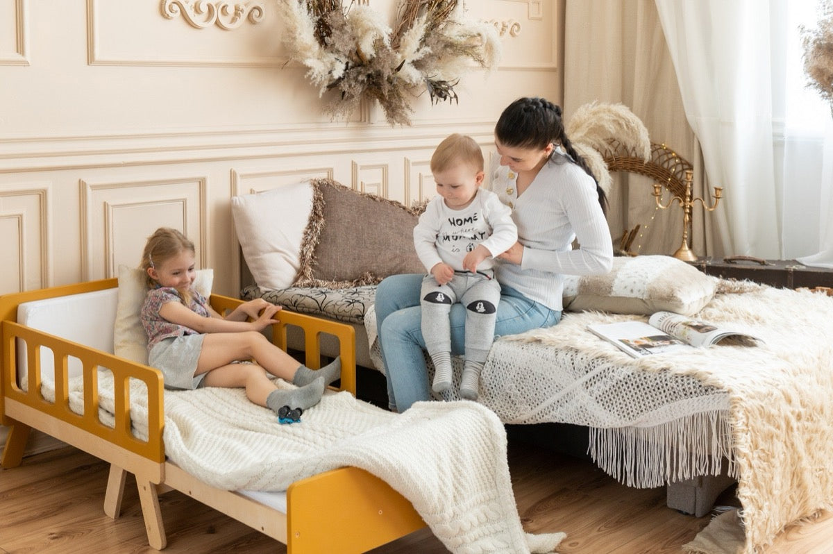 Girl relaxing on yellow Family-scl growing bed next to mother – extendable kids bed in modern bedroom
