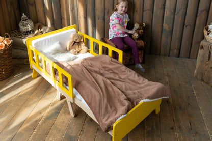 Girl sitting behind yellow Family-scl kids growing bed with teddy bear – wooden children's bed in rustic room