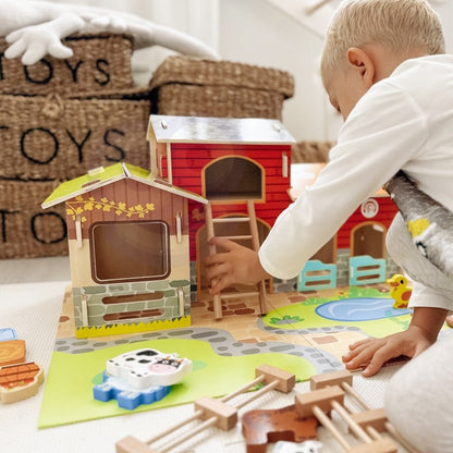 Child's hands exploring wooden barn structures and animal pieces during imaginative farm role-play