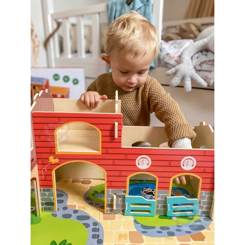 Young child placing wooden animal figurines into red barn structures during hands-on Montessori play