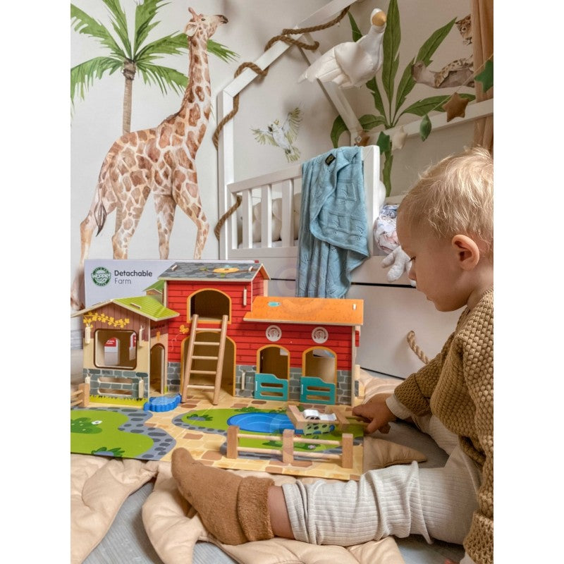 Child manipulating wooden animal figurines and farm building pieces on green play base