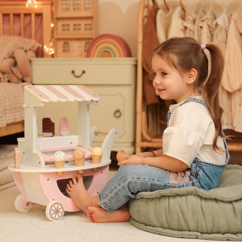 Child seated beside wooden ice cream cart during imaginative role-play session