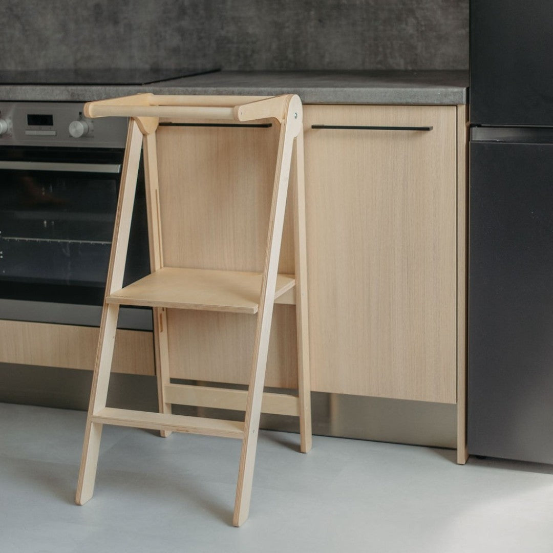 Natural wood foldable kitchen tower partially closed in kitchen showing compact fold-up design with white frame