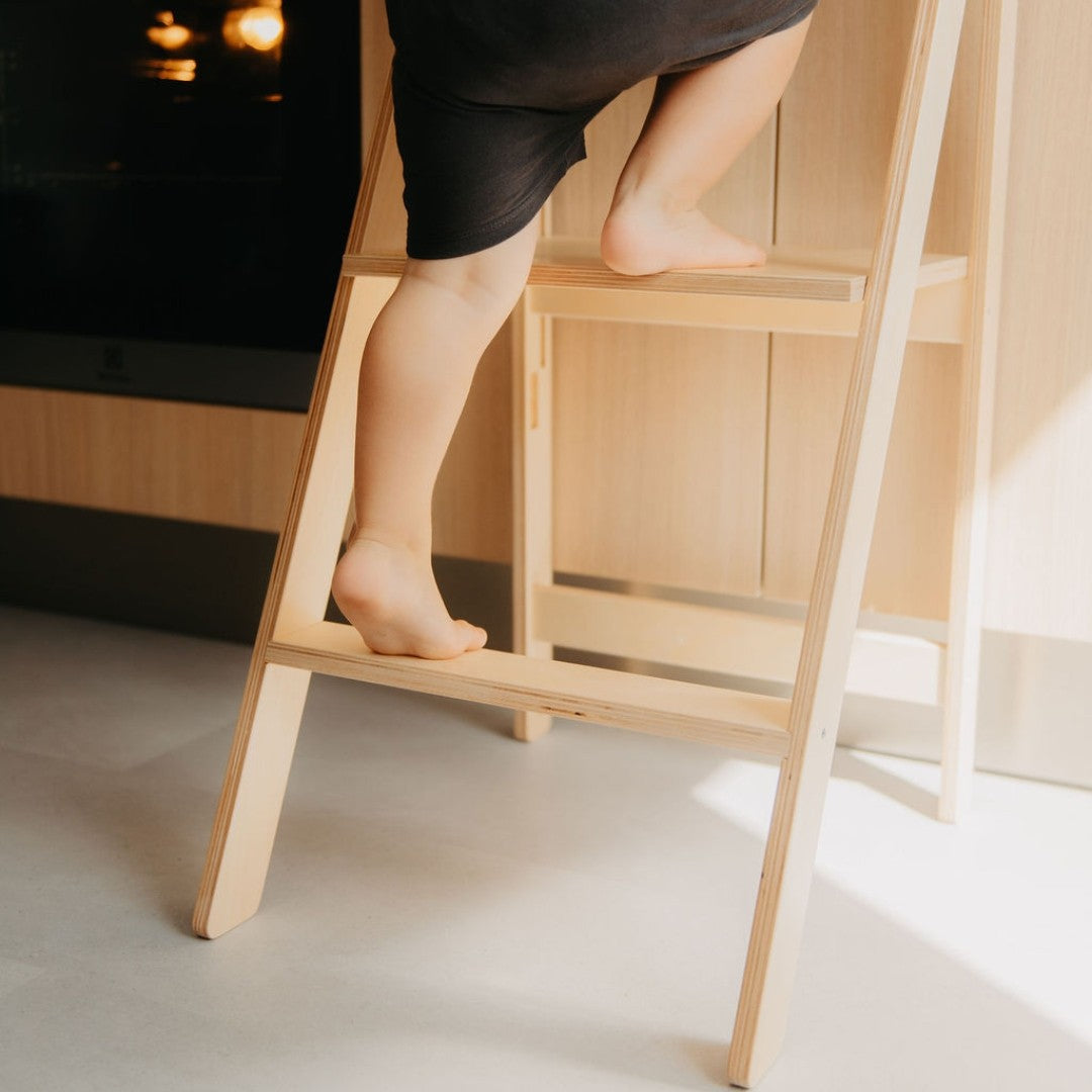 Woman's legs standing on natural wood kitchen tower platform demonstrating safe weight distribution at counter
