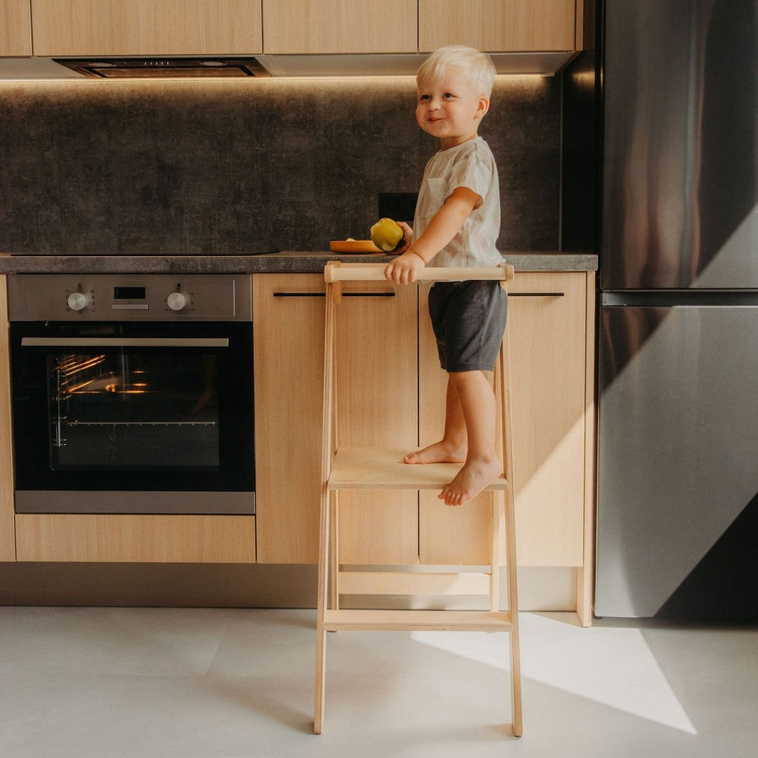 Toddler using kitchen tower to reach sink at standing height with removable safety rail for secure grip