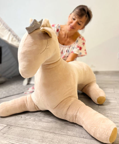 Child playing with large creamy soft toy pegasus with golden crown and extended legs