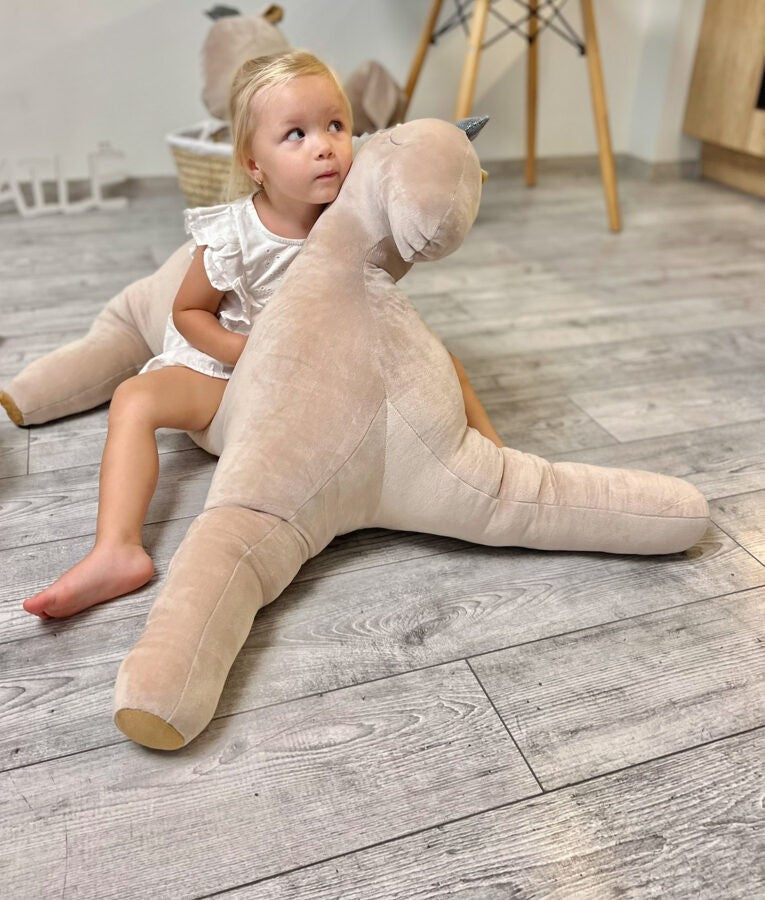 Toddler sitting on large cream soft toy pegasus with gold accents in nursery